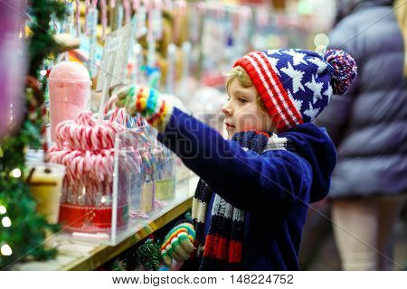 Little cute kid boy near sweet stand with candy canes. Happy child on Christmas market in Germany. Traditional leisure for families on xmas