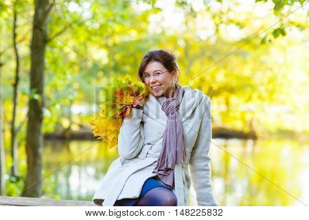Happy young woman with glasses with autumn maple leaves garland in park. Girl enjoying warm october fall day. Beautiful colors and bright light.