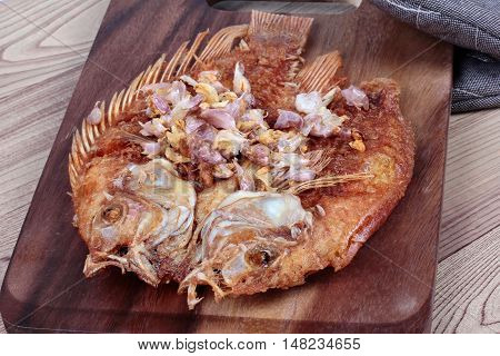 Close up of deep fried fish ,Nile tiapia, with crispy garlic on butcher served. Selective focus.