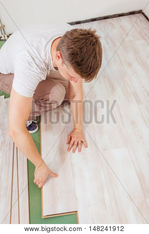 Man installing light laminate flooring in a room