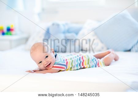 Adorable baby boy in white sunny bedroom. Newborn child relaxing in bed. Nursery for young children. Textile and bedding for kids. Family morning at home. New born kid during tummy time with toy bear.