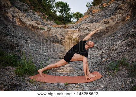 Man doing yoga outdoors. Parshvakonasana. Side view
