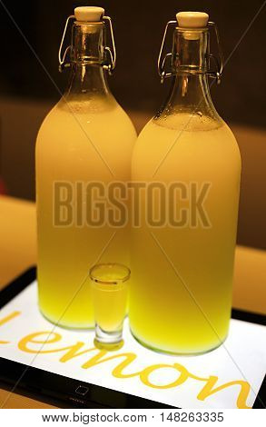 Lemona cocktail in two big bottles and small shot glass on table lighted by tablet underneath in cafe ambient light photo