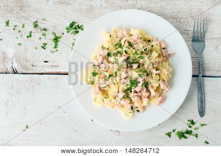 Italian Wholemeal Pasta Tagliatelle with Salmon and Parsley. Fresh pasta with smoked salmon in the sauce on white wooden background with place for text. Italian cuisine concept. Copy space. Top view.