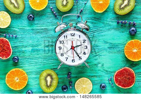 alarm clock - time to breakfast with fruits on green wooden table, mock-up