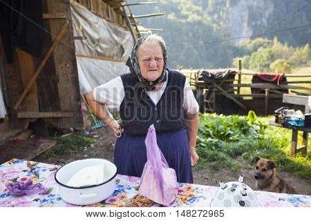 Salciua, Romania - September 14, 2016: Old rural woman selling cheese at the farm in the mountains