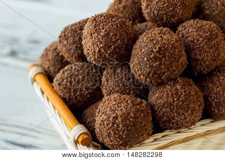 Basket with brown sweets. Little desserts covered in crumbs. Homemade chocolate rum balls. Cocoa powder and biscuits.