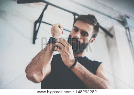 Young Bearded Sportive Man Workout Session Checks Fitness Results Smart Watch.Adult Guy Dress Sport Tracker Wristband Arm.Training hard gym.Horizontal bar background.Blurred