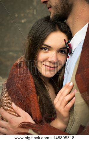 Young fashion elegant stylish couple, Sexy girl looks up and smiles at the camera pressed against the guy, wrarps in pled on streets of old european city