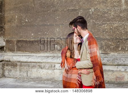Young fashion elegant stylish couple standing, embracing, wrarps in pled on streets of old european city