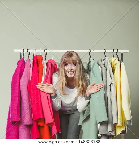 Pretty woman sneaking among clothes in wardrobe. Attractive young girl customer shopping in mall shop. Fashion clothing sale concept.
