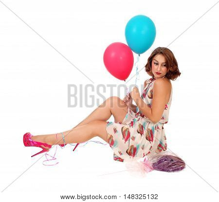 A beautiful young woman sitting on the floor holding two balloons and a lollypop isolated for white background.