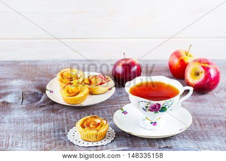 Cup of tea and apple roses shaped muffins on rustic wooden table. Sweet apple dessert pie. Homemade apple rose pastry. Breakfast tea with sweet apple pastry