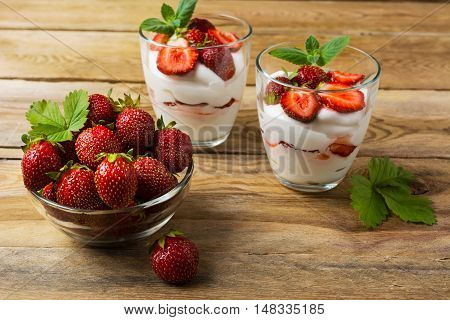 Ripe strawberries and layered cream cheese dessert on wooden background. Whipped cream with fresh strawberry.