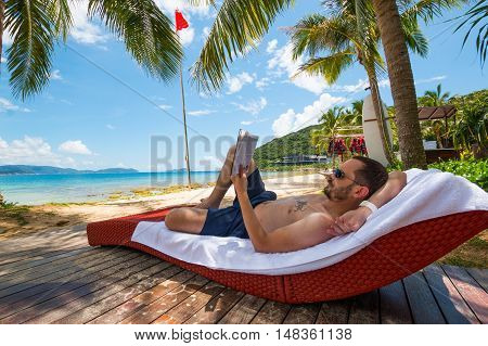Man reading book under oconut palm tree on Beautiful Tropical beach
