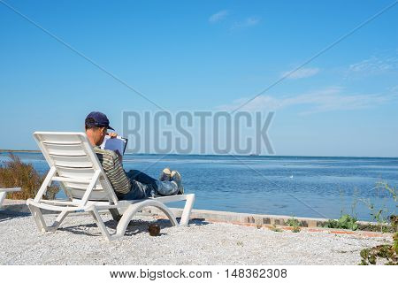 Writer is working on the beach on a sunny day. Back view.