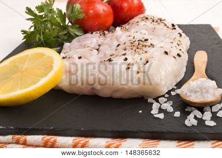 hake fillet on a slate plate with coarse sea salt a slice of lemon parsley and fresh wet tomato