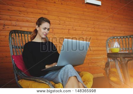 Young confident female entrepreneur remotely is monitoring the execution the work via net-book while is sitting in her home. Woman smart student is using portable laptop computer for on-line learning