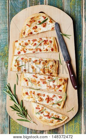 Tart Flambe or Flammkuchen on wooden cutting board. Traditional Alsatian pie. Rustic style, top view.
