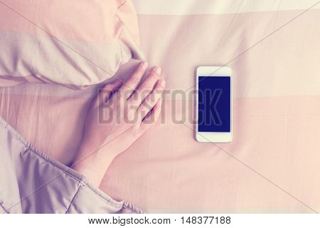 Woman hand under blanket being woken by mobile phone in bedroom.