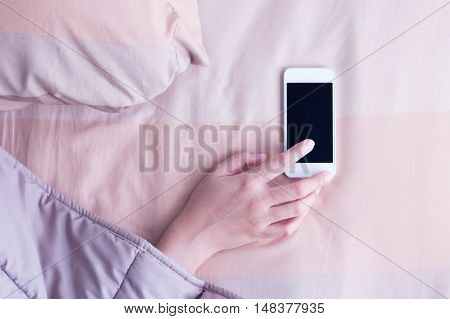 Woman hand under blanket being woken by mobile phone in bedroom.