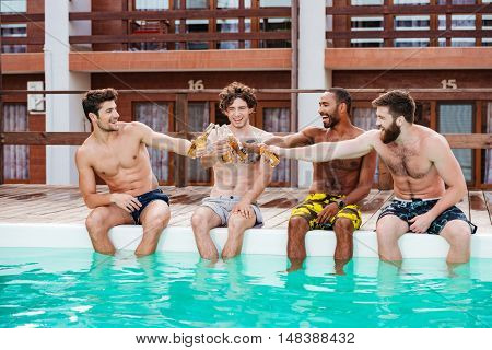 Group of cheerful attractive young men drinking beer and relaxing in swimming pool