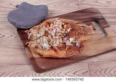 Deep fried fish ,Nile tiapia, with crispy garlic on butcher served. Side view.