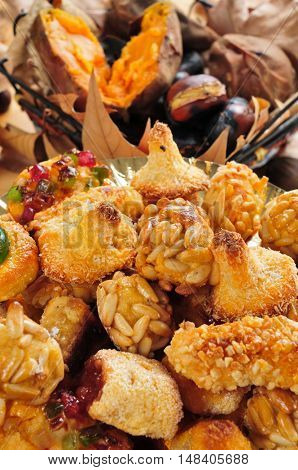 closeup of a plate with Catalan panellets, and some roasted chestnuts and sweet potatoes in the background, as a typical snack in All Saints Day in Catalonia, Spain