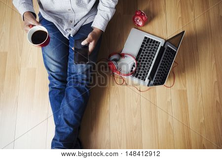 Soft photo of man felling comfort use smartphone on the wooden floor with cup of coffee headphone computer laptop and clock Top view point of copyspace relax time.