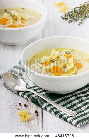 Soup chicken in a white bowl with spoon on a white wooden table.