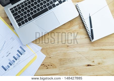 Top View Of Office Wooden Desktop With Analyze Chart, Computer Laptop And Blank White Notebook