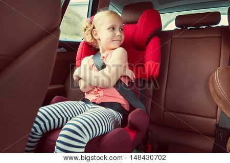 Portrait Of Happy Little Child Girl Sitting Comfortable In Car Seat With Safety Belts Enjoying Ride