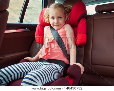 Portrait Of Happy Little Child Girl Sitting Comfortable In Car Seat With Safety Belts Enjoying Ride