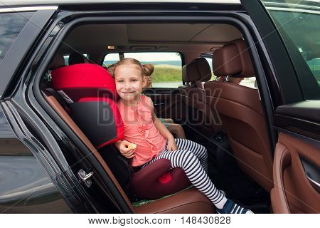 Portrait Of Happy Little Child Girl Sitting Comfortable In Car Seat With Safety Belts Enjoying Ride