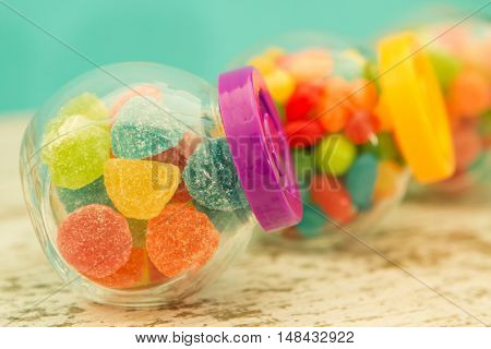 Three glass jars full of jellybeans on wooden table with blue background. Focus in the foreground
