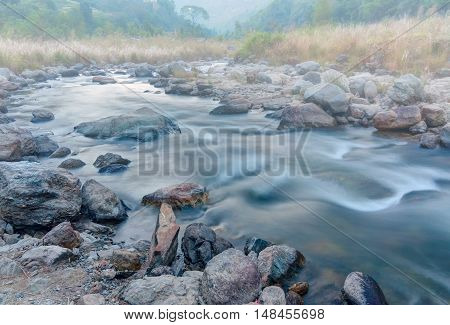 Beautiful Reshi River water flowing through stones and rocks at dawn Sikkim India. Reshi is one of the most famous rivers of Sikkim flowing through the state Shot under fog.