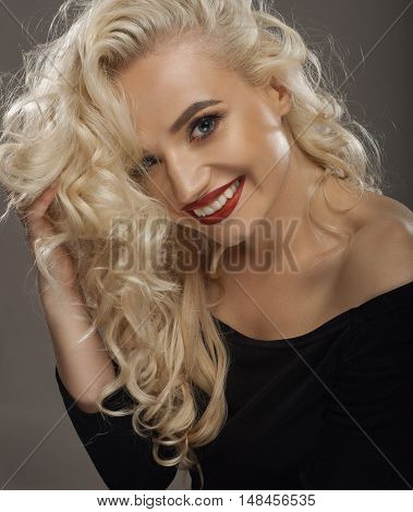 beauty portrait of a positive blond with red lipstick a black shirt holding a hand hair