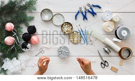 Making handmade christmas balls. Woman's leisure, tools for creating holiday decorations and garland. Top view of white wooden table with female hands holding various trinkets, decor accessories