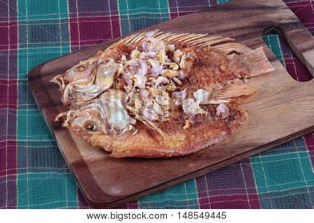 Deep fried fish ,Nile tiapia, with crispy garlic on butcher served. Side view.
