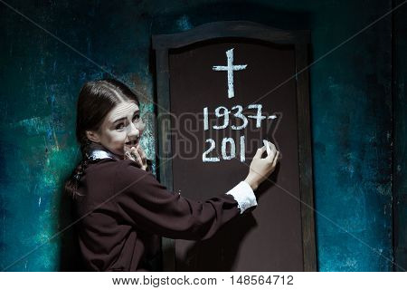 Halloween theme: Portrait of a young smiling girl in school uniform as killer woman against school board . The image in the style of Halloween and Addams family