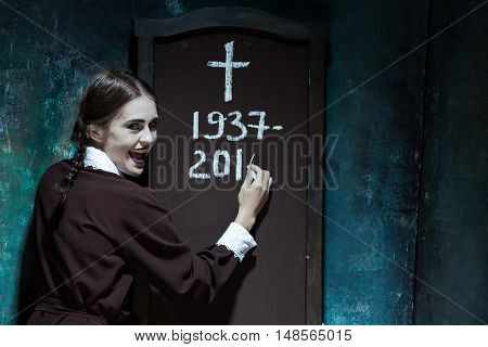 Halloween theme: Portrait of a young smiling girl in school uniform as killer woman against school board . The image in the style of Halloween and Addams family
