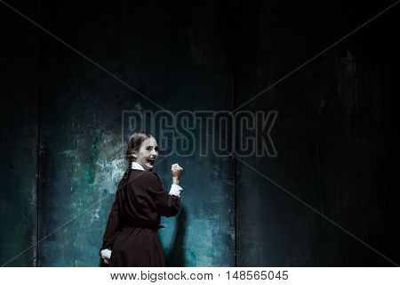 Halloween theme: Portrait of a young smiling girl in school uniform as killer woman against school board . The image in the style of Halloween and Addams family