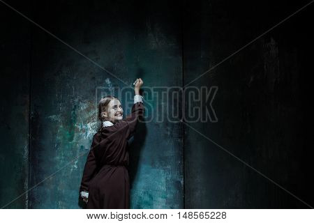 Halloween theme: Portrait of a young smiling girl in school uniform as killer woman against school board . The image in the style of Halloween and Addams family