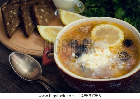Solyanka - Russian traditional meat soup with hot spices in a bowl with bread and spoons on old wooden background. Close up. Meat solyanka - traditional Russian dish. Russian cuisine concept.