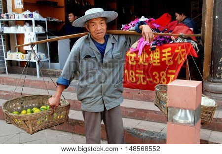 Luo Dai China - October 13 2007: Street vendor carrying baskets filled with oranges suspended from a shoulder yoke