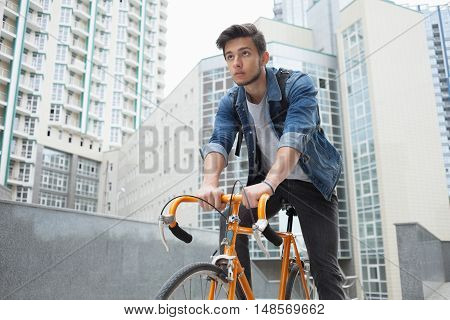 A guy in a blue denim jacket on orange bicycle. Man on the background of the city with a backpack on a bike