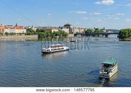 View of the Vltava river with cruise tour boats from the Charles Bridge. The National Theatre and the Legion bridge are seen. Prague Czech Republic.