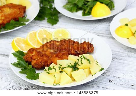 Wiener schnitzel and boiled potatoes with chopped chives sliced lemon and lettuce