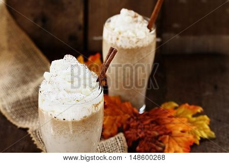 Pumpkin Spice Iced Coffee with whipped cream and cinnamon against a rustic background. Shallow depth of field with selective focus on Latte in foreground.
