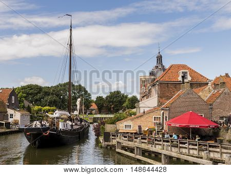 Enkhuizen The Netherlands - August 9 2016: Ship in the harbor of Enkhuizen with old houses drommedaris and terrace with people.